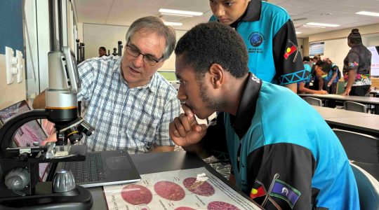 School students and researcher studying microscope. | Newsreel