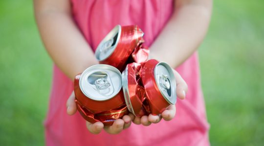 Girl holding crushed cans. | Newsreel