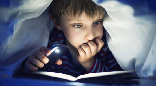 Boy reading book under bed covers. | Newsreel