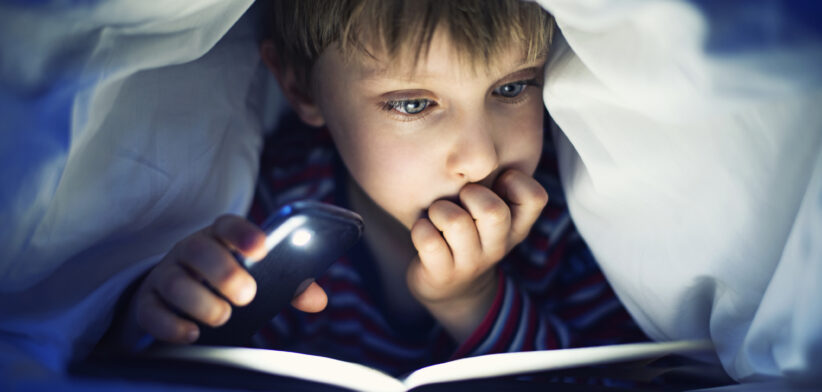 Boy reading book under bed covers. | Newsreel