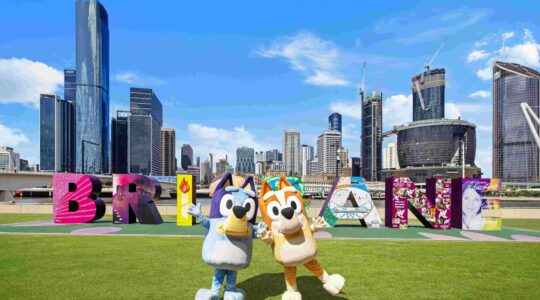 Animated character Blue in front of Brisbane sign