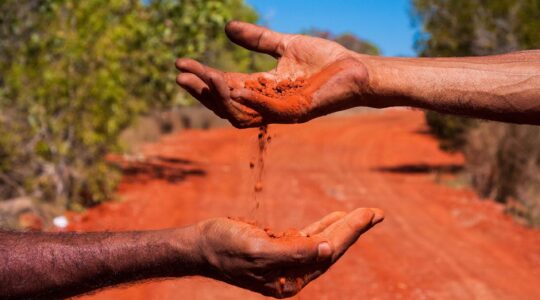 Two hands in Australian outback with red dirt. | Newsreel