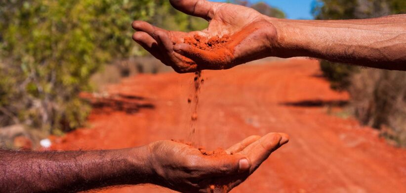 Two hands in Australian outback with red dirt. | Newsreel