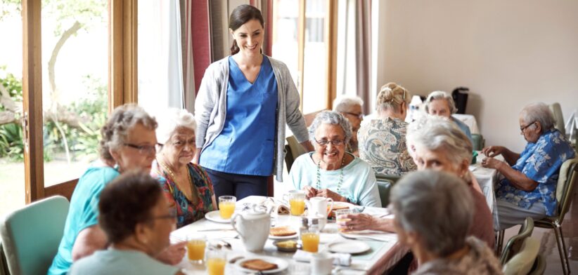 Carer with elderly in aged care home dining room. | Newsreel