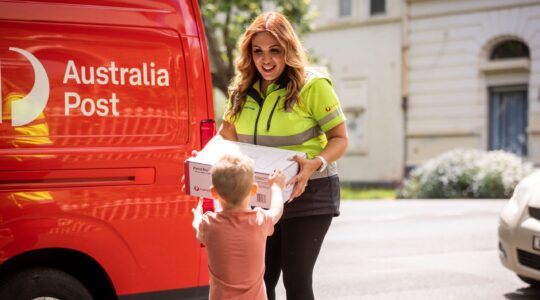 Australia Post delivery woman handing parcel to child.