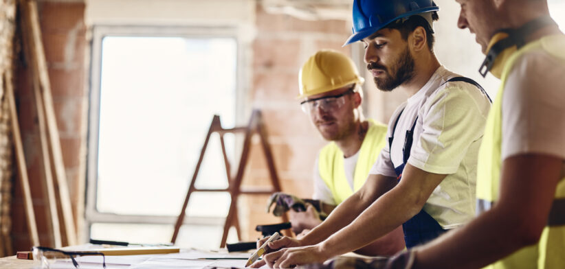 Team of manual workers examining housing project while working at construction site.