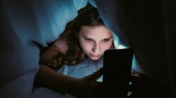 Girl viewing phone under bed covers. | Newsreel