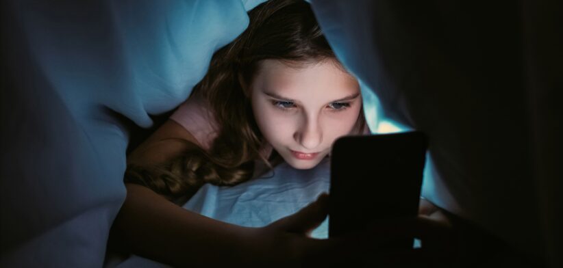 Girl viewing phone under bed covers. | Newsreel