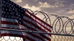 Unites States flag with barbed wire in front.| Newsreel