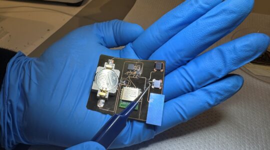 A hand wearing blue gloves holding a compact electronic sensor, developed for monitoring wound healing. | Newsreel