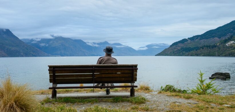 Man sitting on the bench, enjoying the views of Lake Wakatipu and mountain ranges. Queenstown. New Zealand. | Newsreel