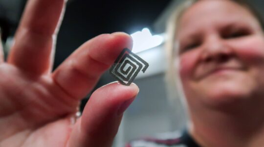 A woman holds a small square spiral-shaped diamond–titanium device between her fingers. | Newsreel