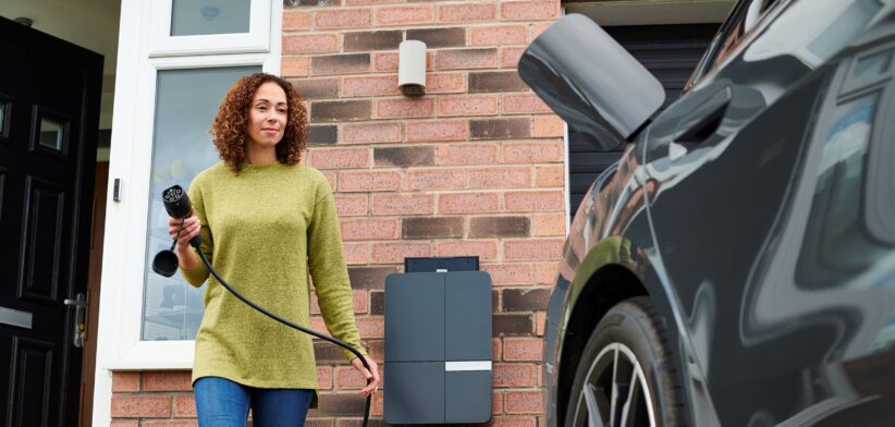 Woman charging electrics vehicle in driveway. | Newsreel