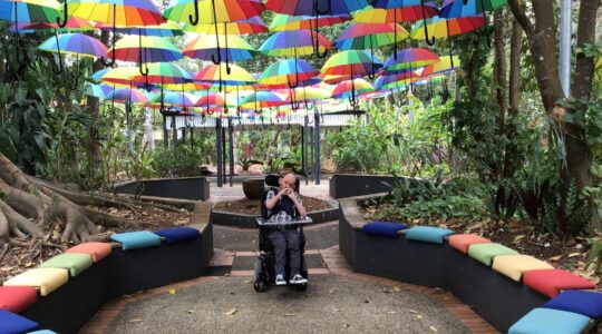Person on wheelchair under umbrellas. | Newsreel