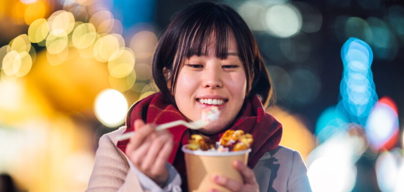 Young woman enjoying eating sweet food at Christmas market