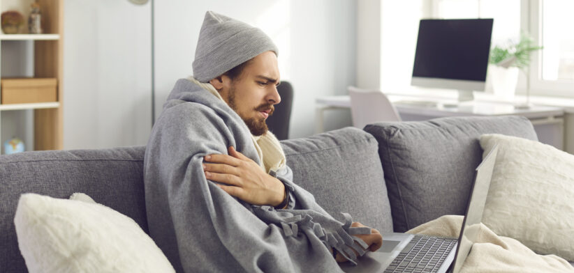 Young man having fever and chills, listening to eHealth doctor or looking for health advice online