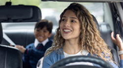 Happy mother picking up her son from school in her car