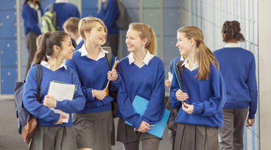 Cheerful female students wearing blue school uniforms walking in locker room