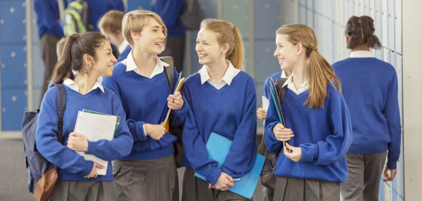 Cheerful female students wearing blue school uniforms walking in locker room