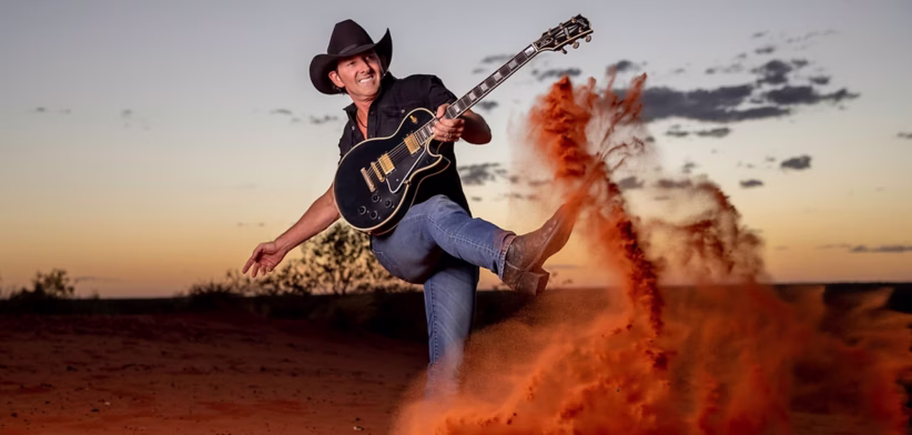 Man with guitar kicking up red dust in bush - Newsreel