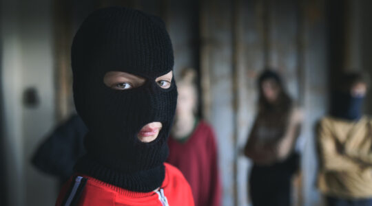 Boy with mask with teenagers gang indoors in abandoned building, looking at camera.