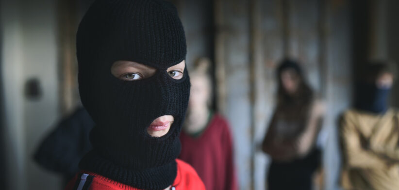 Boy with mask with teenagers gang indoors in abandoned building, looking at camera.