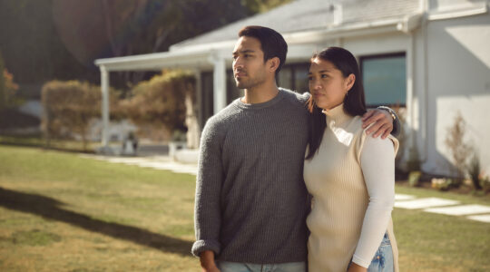 A Serious Couple Standing by Their Home