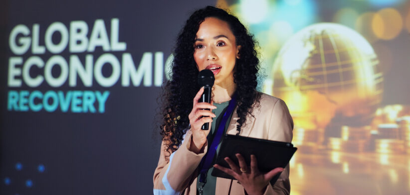 Woman, seminar and tablet at convention, stage or discussion with mic for global economy recovery. Person, analyst and event for speech, info and feedback at international conference for presentation