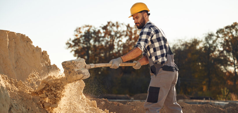 The soil, digging with shovel. Worker is on the construction site at daytime