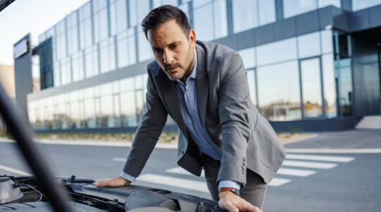 Businessman having car trouble looking at engine