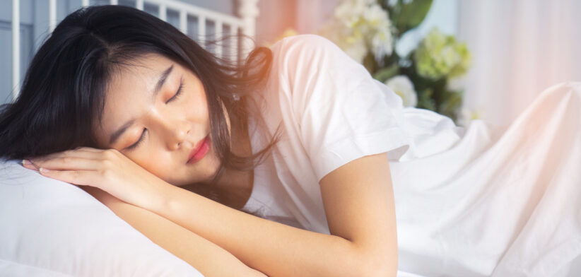 Woman stretching in bed after waking up, back view. Woman sitting near the big white window while stretching on bed after waking up with sunrise at morning, back view.