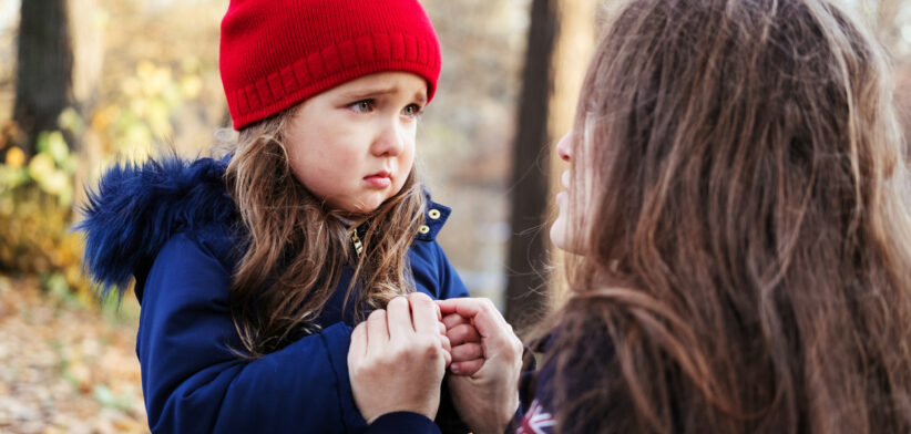 Scared daughter holding mother’s hands in autumn park. Child girl express sad emotions, complain about their own problems