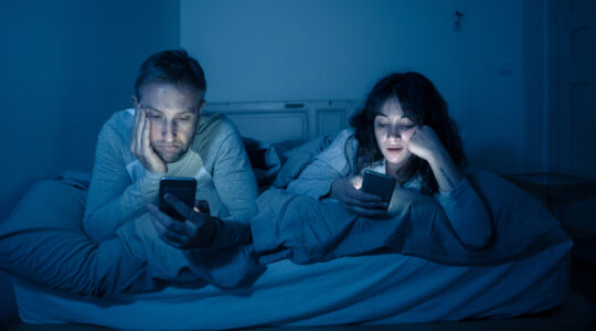 Life style portrait of young bored couple in bed at night on smart phones obsessed with games, social media, apps ignoring each other. Relationship communication problems and phone addiction concept.