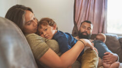 Shot of a little boy resting on his mother’s chest with his baby brother and father in the background