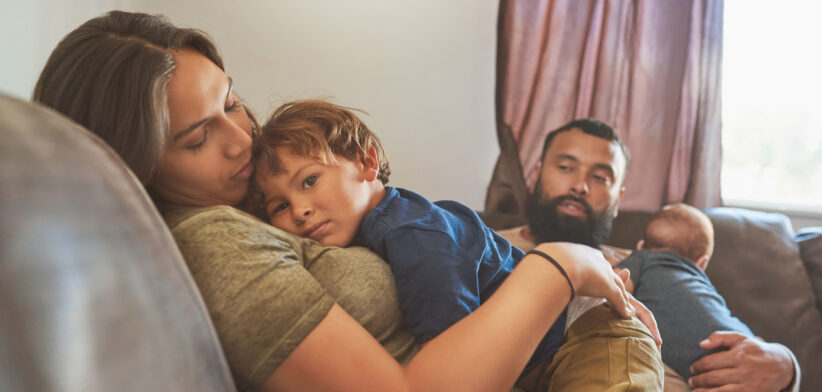 Shot of a little boy resting on his mother’s chest with his baby brother and father in the background
