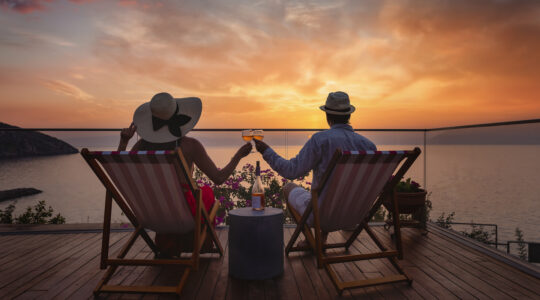 A romantic couple sitting in lounge chairs on summer vacation enjoys the sunset