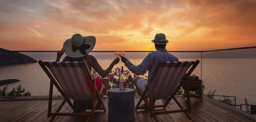A romantic couple sitting in lounge chairs on summer vacation enjoys the sunset
