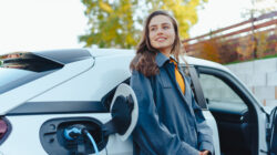 Young woman waiting while her electric car charging in home charging station, sustainable and economic transportation concept.