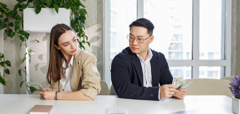 Man and woman sitting in office, holding money at hands. Gender pay gap, unequal salary concept