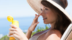 Woman with straw hat applying sunblock to face outdoors