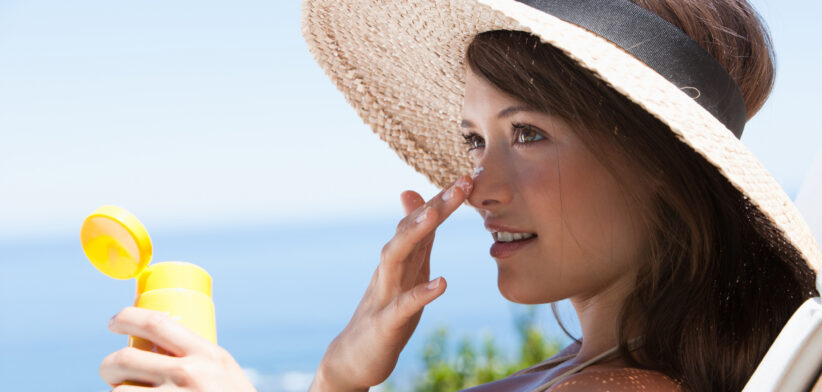 Woman with straw hat applying sunblock to face outdoors