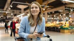 Attractive woman searching for food in a supermarket from a checklist on her phone
