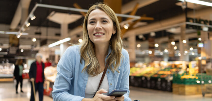 Attractive woman searching for food in a supermarket from a checklist on her phone