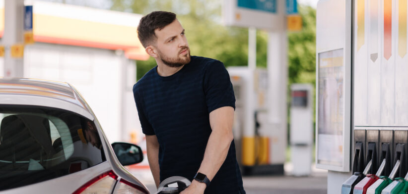 Bearded man refuelling car on gas station and looking into his smartphone. Man compares fuel prices