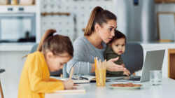 A busy working mother having a work-related video call at home on her laptop and looking after her children