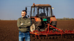 Portrait of satisfied mature farmer standing in field preparing to cultivate the land with a tractor.