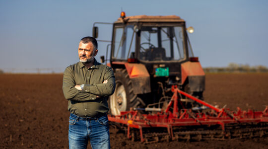 Portrait of satisfied mature farmer standing in field preparing to cultivate the land with a tractor.