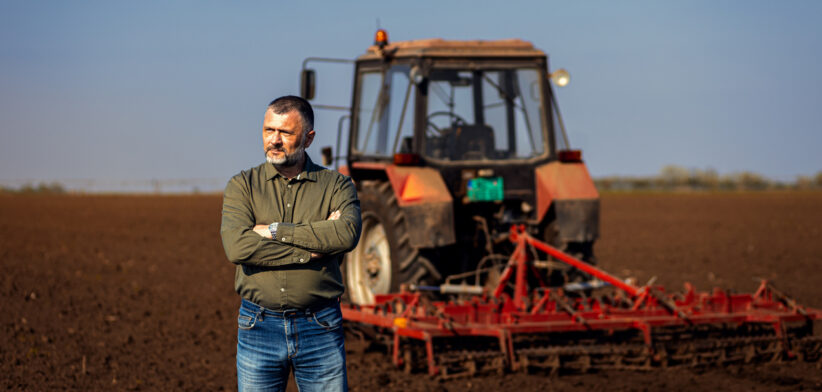 Portrait of satisfied mature farmer standing in field preparing to cultivate the land with a tractor.