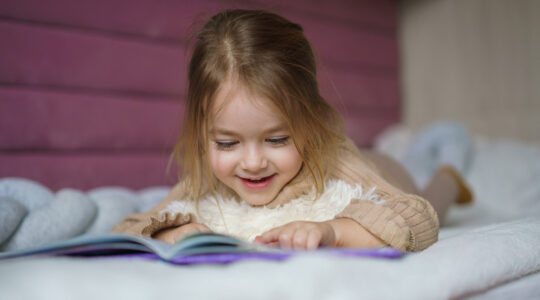 Girl lying in bed and looking at picture book