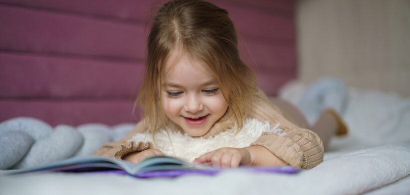 Girl lying in bed and looking at picture book